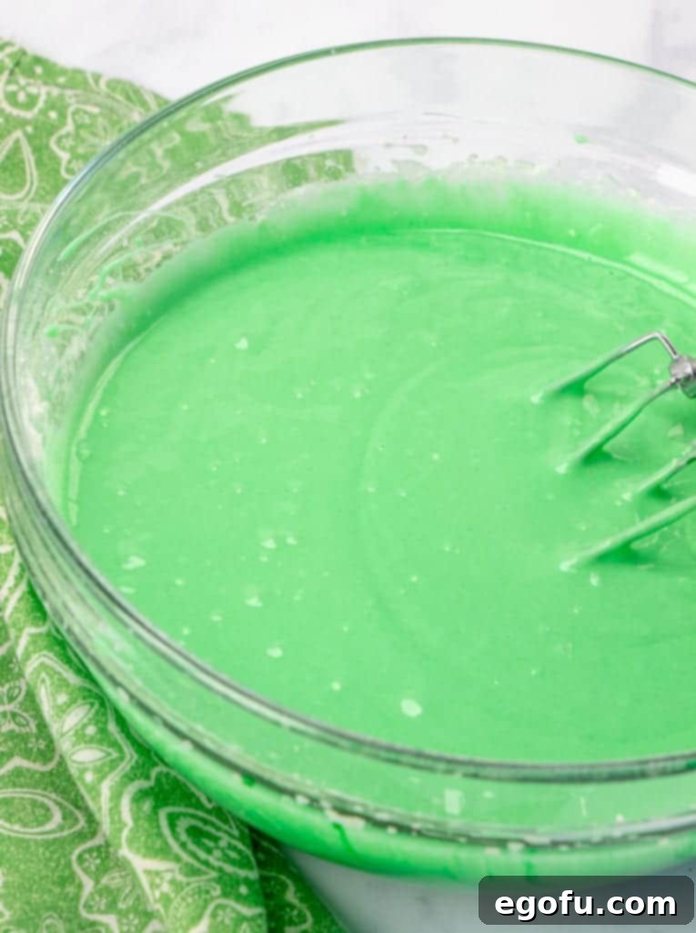 Effortless Grasshopper Indulgence 6 Green food coloring being mixed into the cake batter with an electric mixer, creating a vibrant green color.