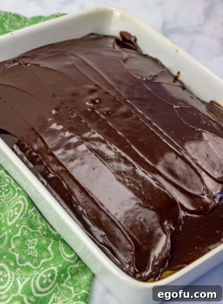 Effortless Grasshopper Indulgence 8 Rich hot fudge sauce being meticulously spread over the fully cooled, baked green cake, forming an even layer.