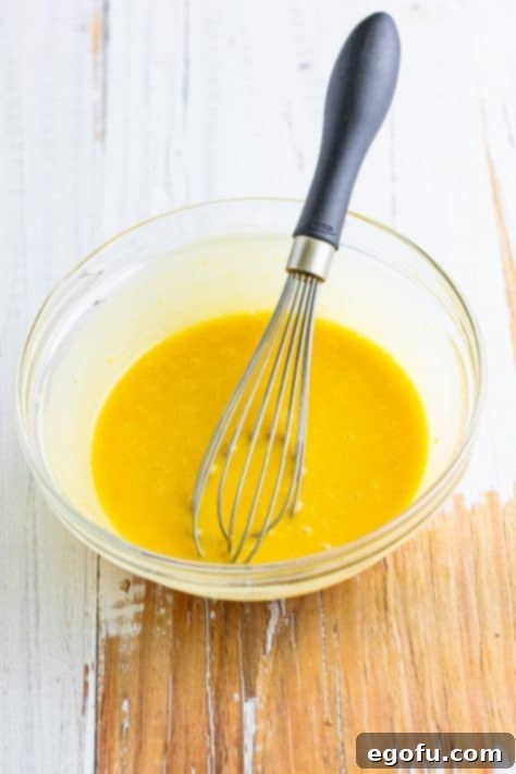 A whisk in a bowl of Honey Mustard.