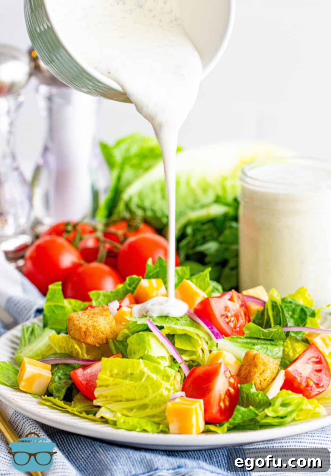 Handcrafted Ranch Bliss 2 homemade ranch dressing shown being poured onto a fresh salad on a white plate.