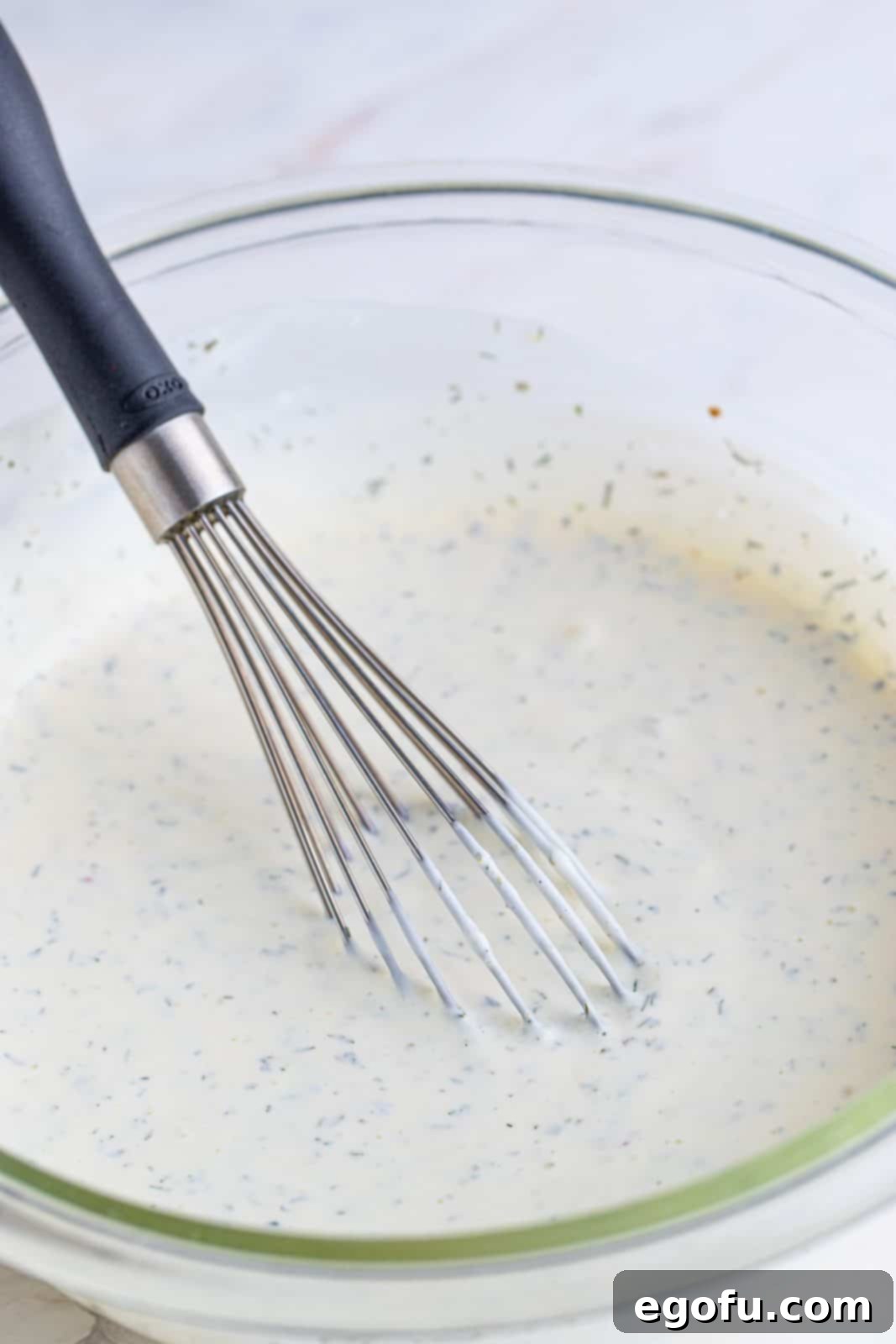 Handcrafted Ranch Bliss 7 fully whisked together ranch dressing ingredients shown in a clear bowl with a silver whisk.