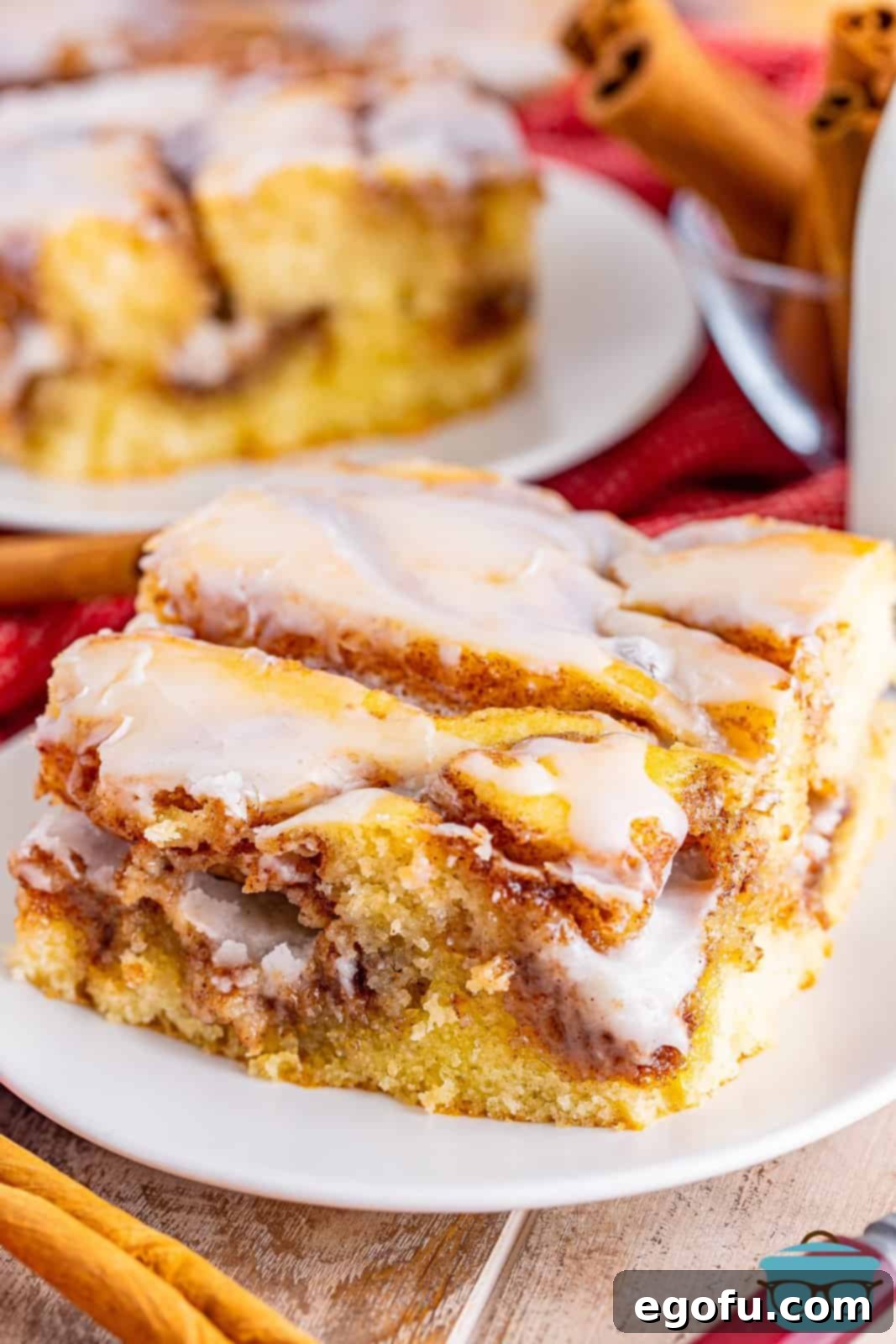 Swirl of Spice Cake 2 A perfectly sliced piece of homemade Cinnamon Roll Cake, adorned with vanilla icing, resting on a small round white plate.