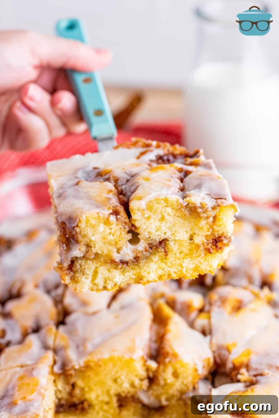 Swirl of Spice Cake 14 A spatula gently lifts a slice of the magnificent Cinnamon Roll Cake, revealing its luscious layers and inviting texture, over the remaining cake in the baking dish.