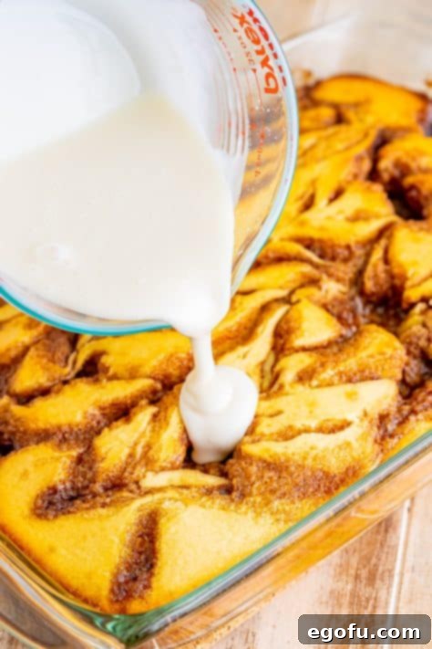 Swirl of Spice Cake 25 A generous cascade of sweet vanilla glaze is being poured over the warm, freshly baked Cinnamon Roll Cake, promising a delightful finish.