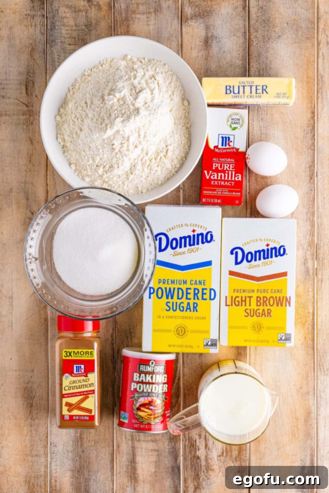 Swirl of Spice Cake 4 An array of ingredients for Cinnamon Roll Cake, neatly displayed: all-purpose flour, granulated sugar, baking powder, eggs, vanilla extract, milk, salted butter, light brown sugar, cinnamon, and powdered sugar.