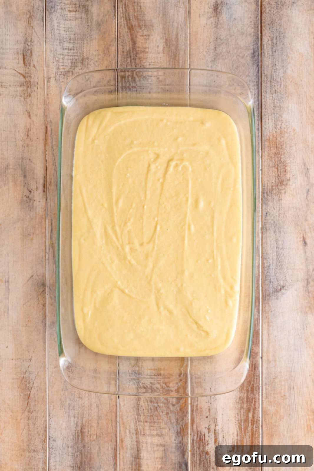 Swirl of Spice Cake 7 Smooth, uncooked cake batter is evenly spread across the bottom of a Pyrex baking dish, forming a perfect base for the cinnamon swirl.