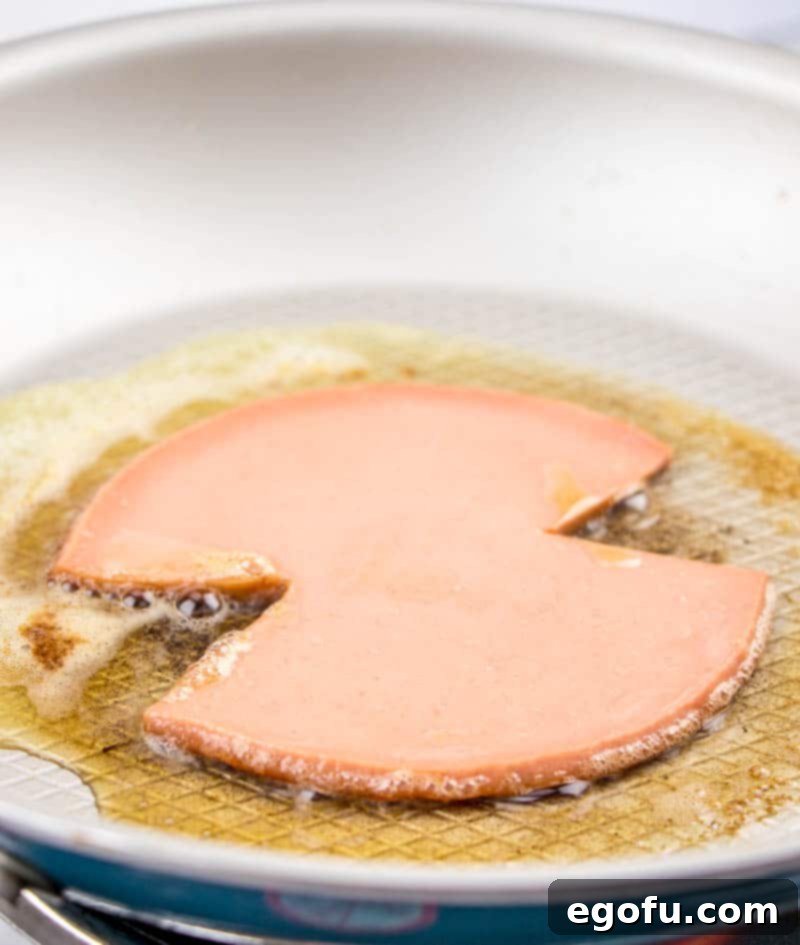 Thick-cut bologna sizzling in a hot frying pan with melted butter, beginning to crisp and brown along the edges, ready for a classic sandwich.