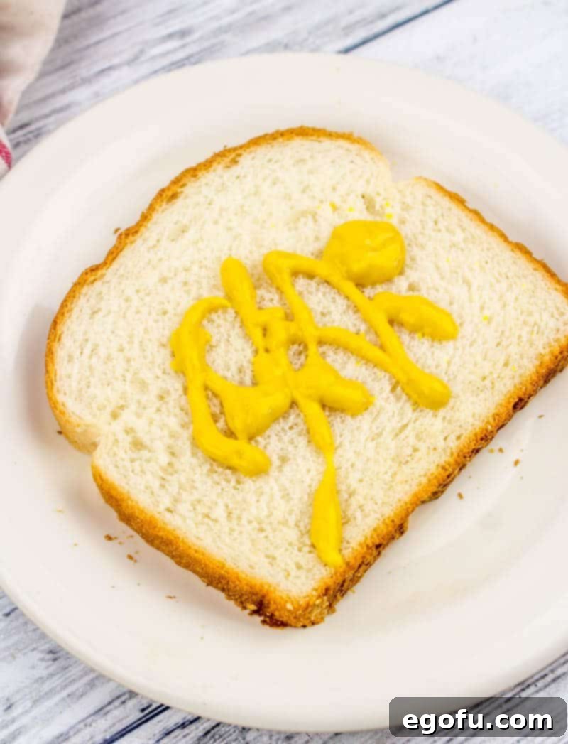 Soft white bread generously spread with bright yellow mustard, the perfect base for a classic fried bologna sandwich.
