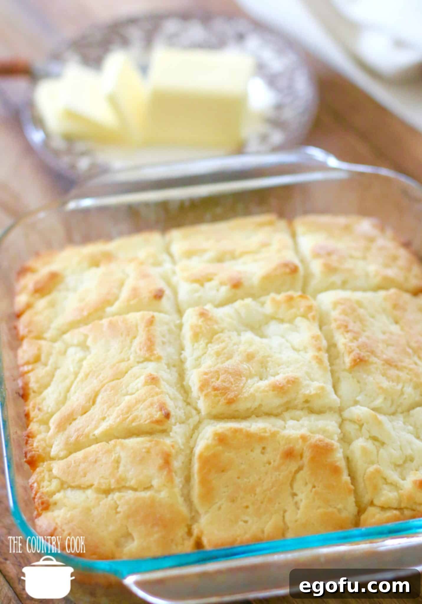 Golden Butter Biscuits 12 Butter Dip Buttermilk Biscuits recipe, no biscuit cutters, in a square Pyrex baking dish with sliced butter in the background.