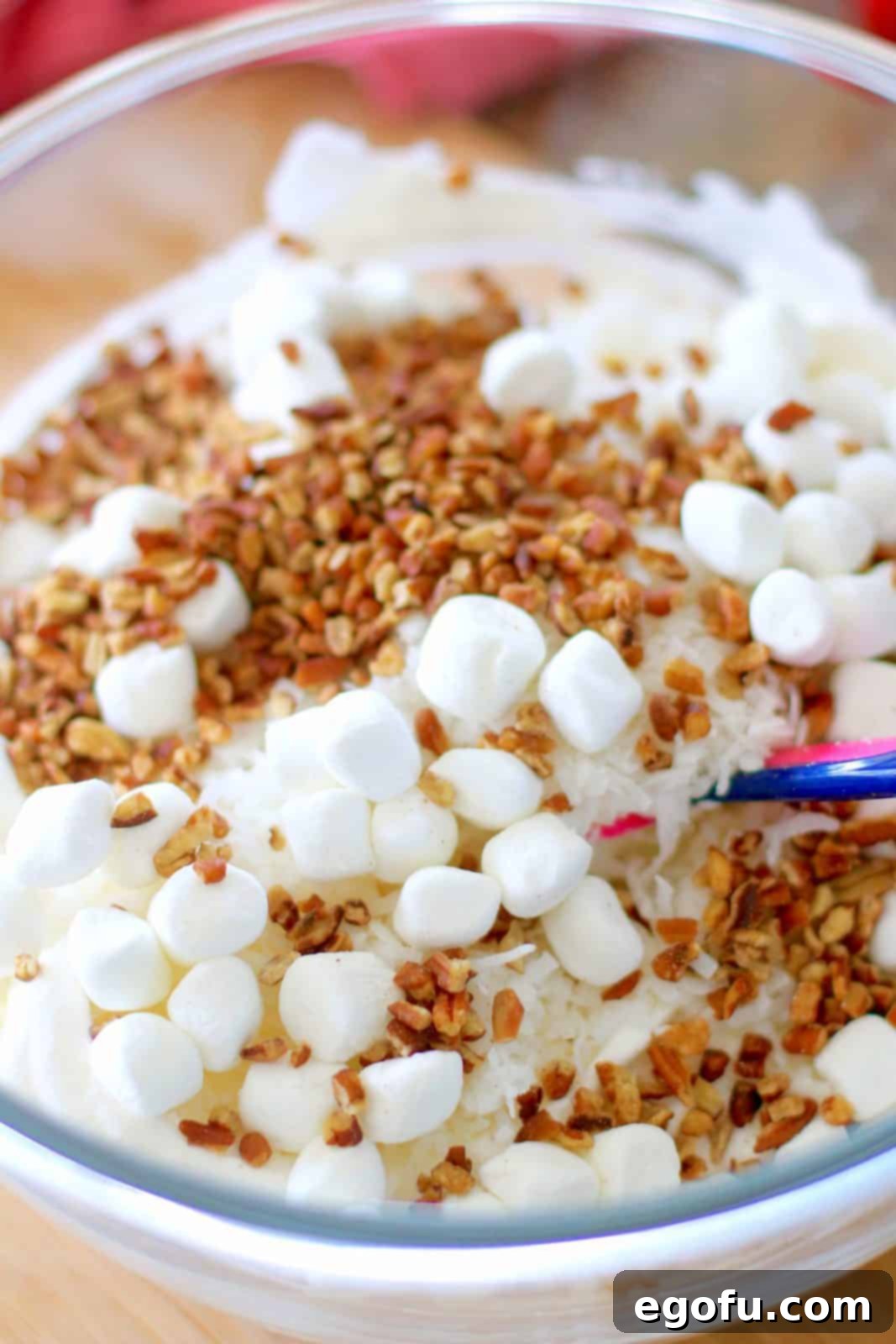 Southern Ambrosia Delight 6 Mini marshmallows, chopped pecans, shredded coconut added to sour cream and cool whip in a large clear bowl.