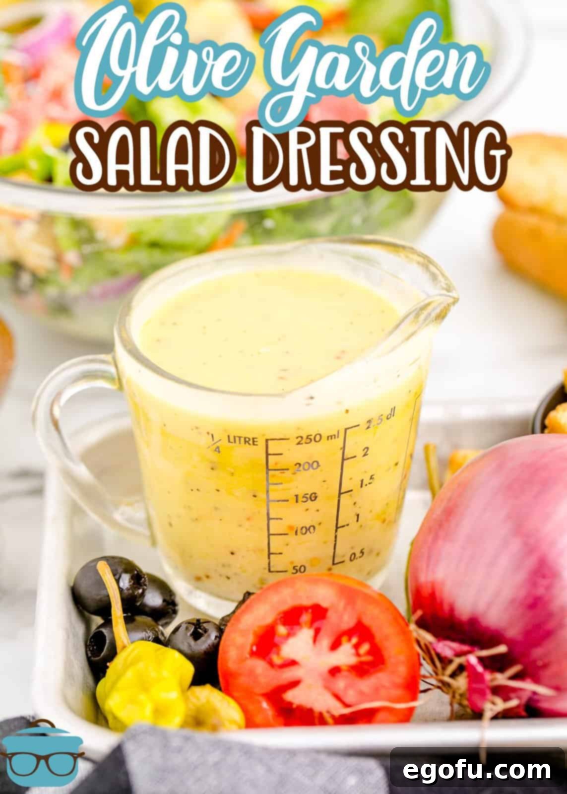 A measuring cup filled with homemade Olive Garden Salad Dressing, with a fresh salad blurred in the background.