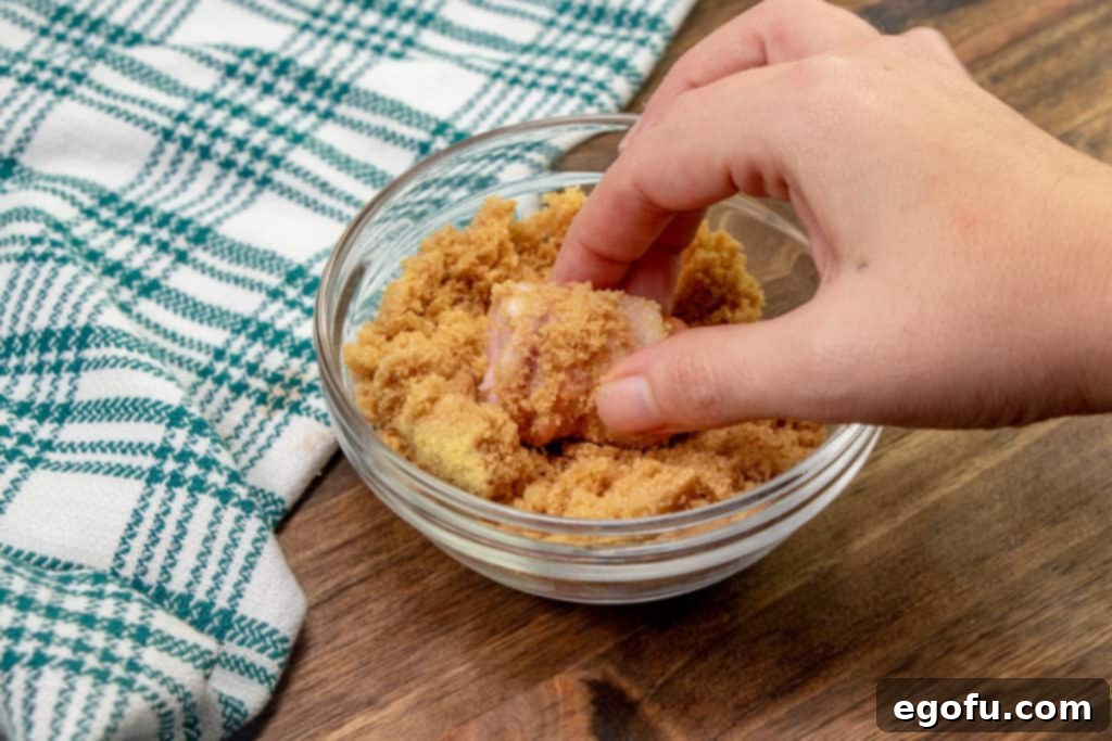 Crispy Bacon Brat Poppers 8 rolling bacon wrapped bratwurst in brown sugar mixture, preparing for baking