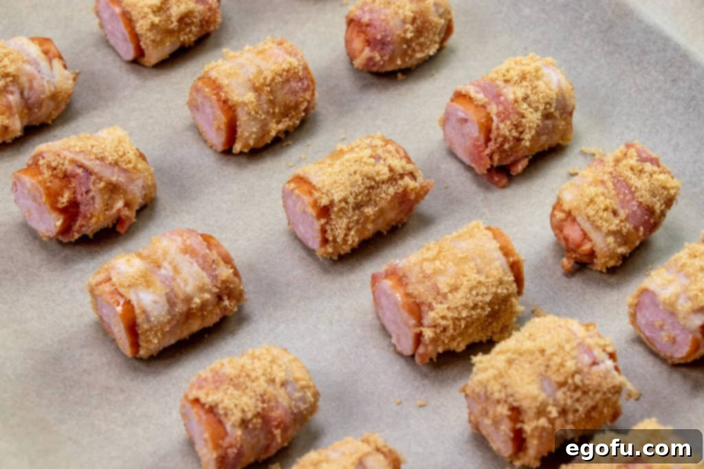 Crispy Bacon Brat Poppers 9 bacon wrapped brats arranged on a baking tray covered with parchment paper, ready for the oven