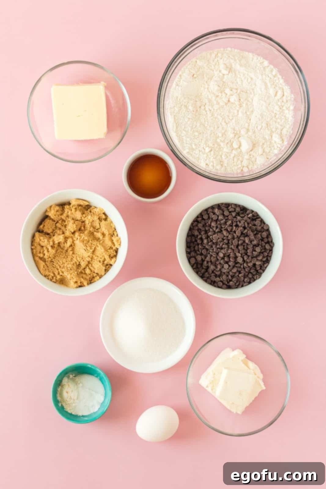 A flat lay photograph showcasing all the ingredients required for making Chocolate Chip Cream Cheese Cookies: unsalted butter, softened cream cheese, light brown sugar, granulated sugar, a large egg, vanilla extract, all-purpose flour, baking soda, cornstarch, salt, and a generous bowl of mini semi-sweet chocolate chips.
