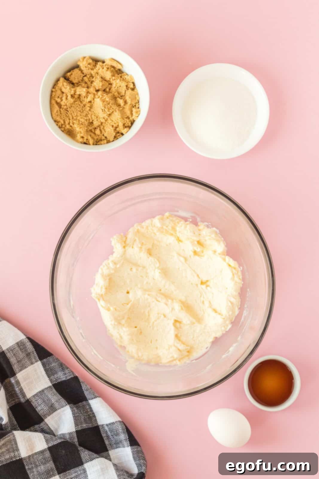 A close-up shot of butter and cream cheese being beaten together in a large mixing bowl, forming a smooth, creamy mixture.