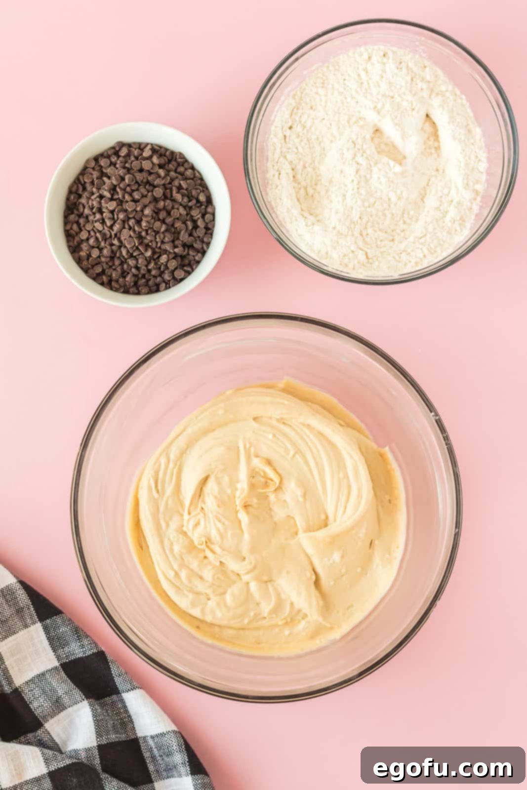 Brown sugar, granulated sugar, a cracked egg, and vanilla extract being added to and beaten into the creamy butter and cream cheese mixture in a bowl.