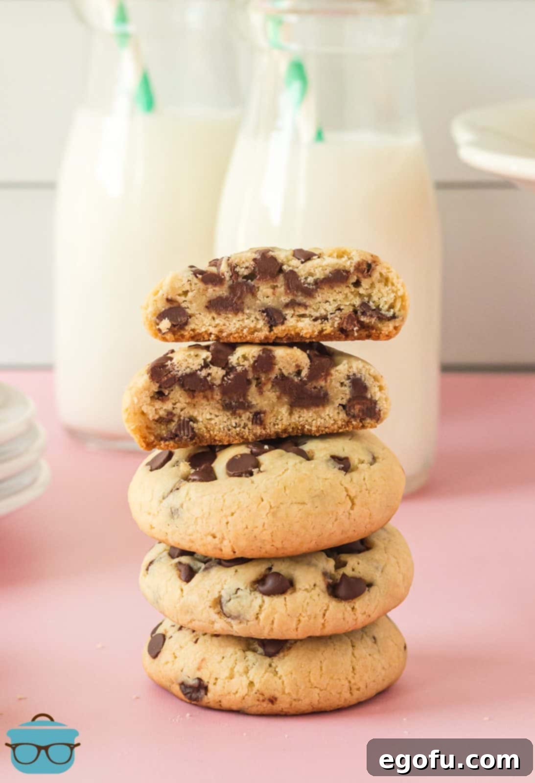 A stack of freshly baked Chocolate Chip Cream Cheese Cookies with the top cookie broken in half, revealing its soft, chewy interior and abundant mini chocolate chips.