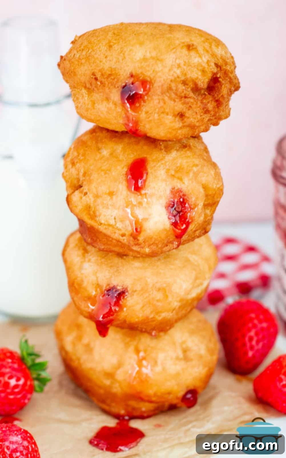 Stacked Strawberry Jelly Filled Biscuit Donuts on top of one another with strawberries surrounding them.