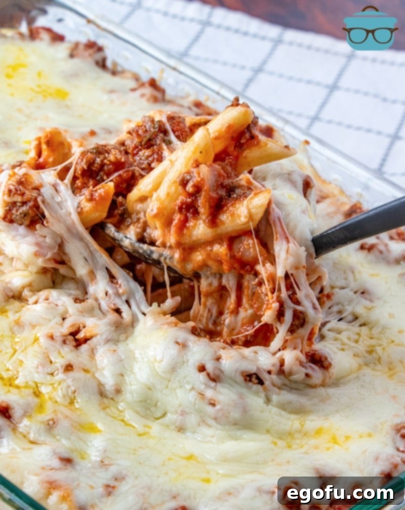 A baking dish of freshly baked ziti, with a serving spoon scooping out a portion, ready to be enjoyed.