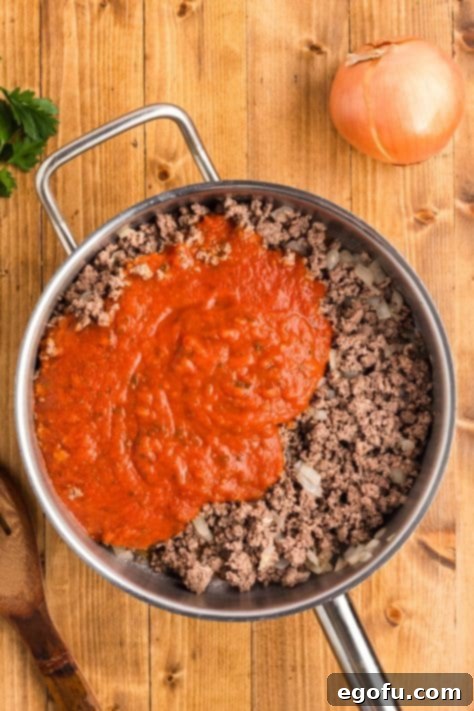 pasta sauce poured over cooked ground beef and onion in a skillet.
