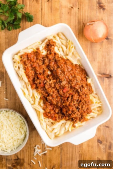 ground beef pasta sauce poured over penne pasta in baking dish.