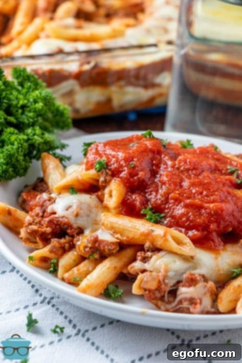 a white plate of baked ziti with extra sauce on top.