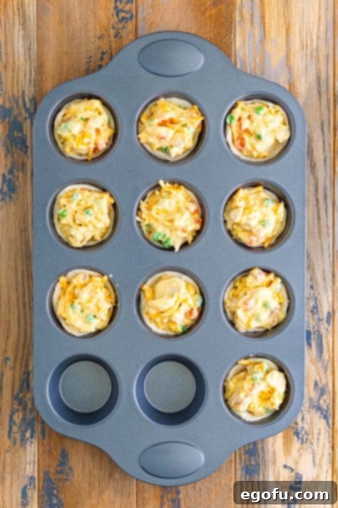 A muffin pan with unbaked Mini Chicken Pot Pies with shredded cheese on top.
