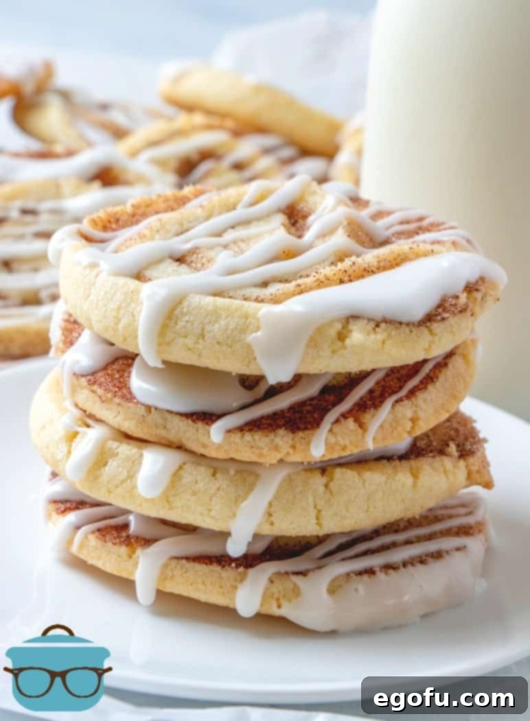 Easy Cinnamon Roll Cookies stacked four cookies high on a white plate surrounded by additional cookies, inviting indulgence.
