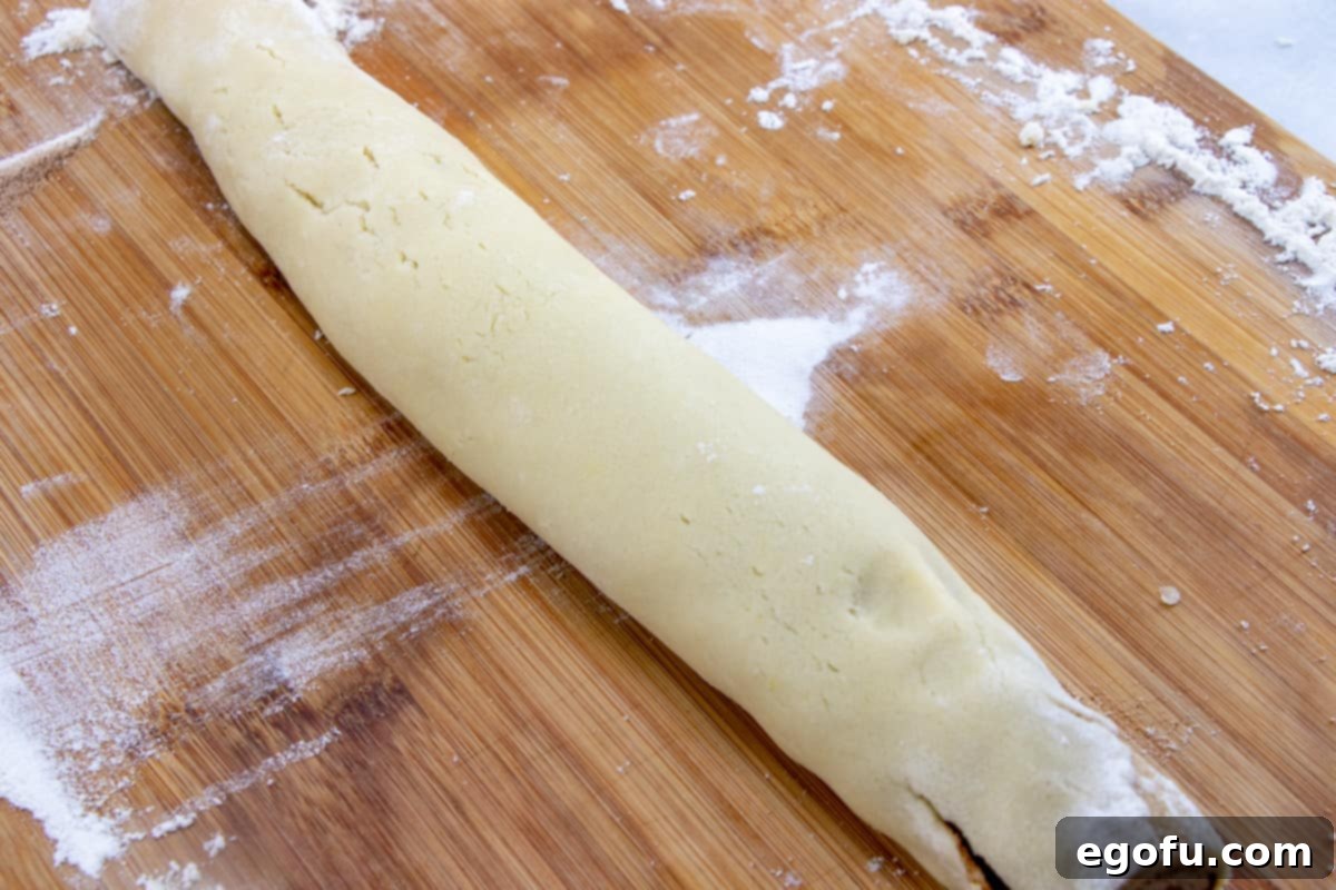 Rolled up cinnamon roll cookie dough log on a large cutting board, ready for chilling.