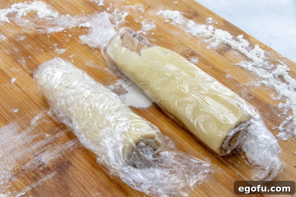 Cinnamon roll cookie dough cut in half and wrapped in plastic wrap, ready for the freezer.