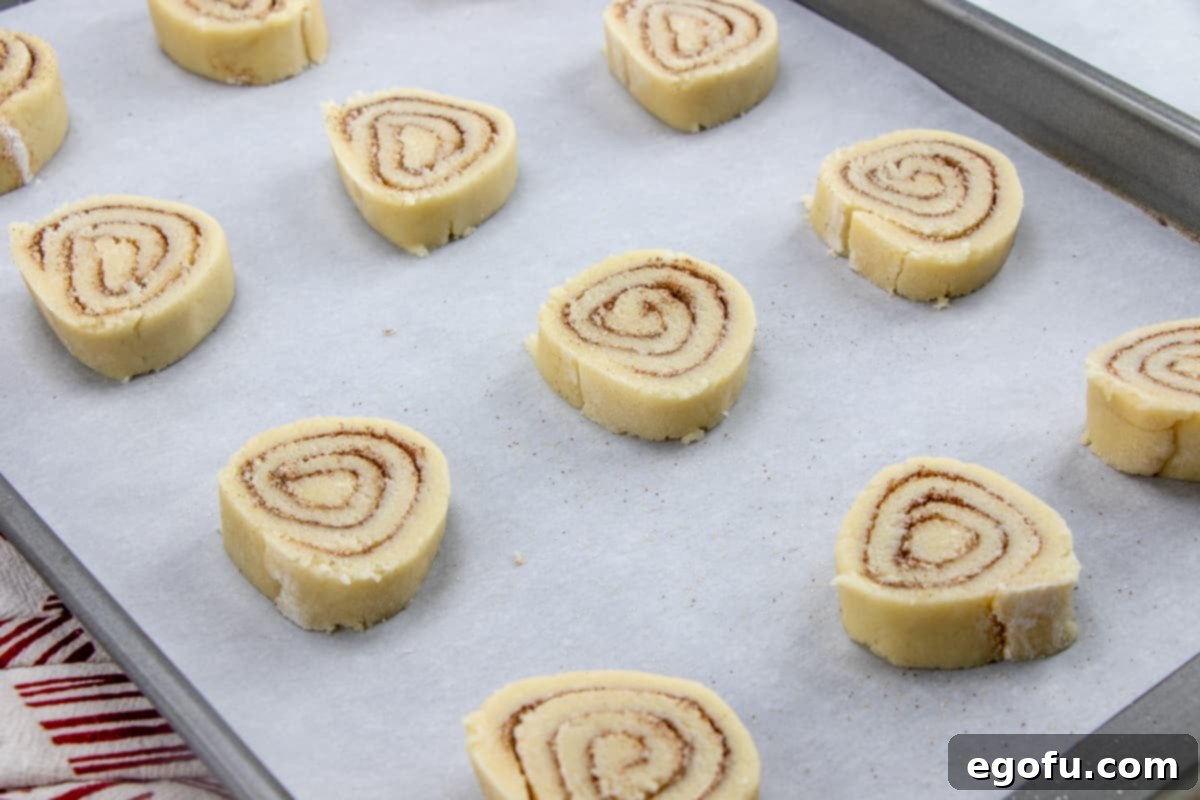 Sliced cinnamon roll cookie dough on parchment paper covered baking sheet, spaced for even baking.