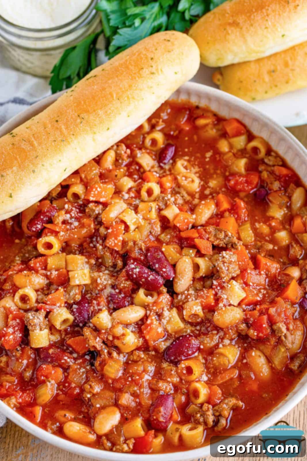 an overhead photo of pasta e fagioli in a white bowl with a breadstick on the side.