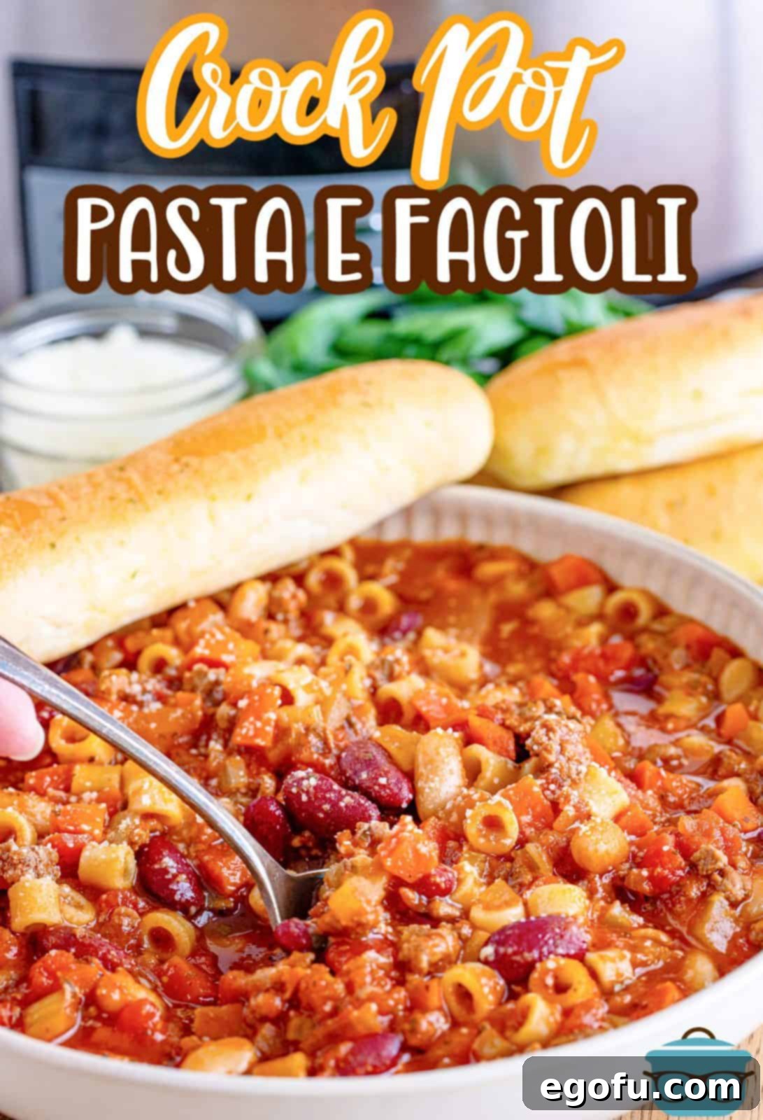 Crock Pot Pasta e Fagioli shown in a white bowl with a spoon and a piece of garlic bread on the side. 