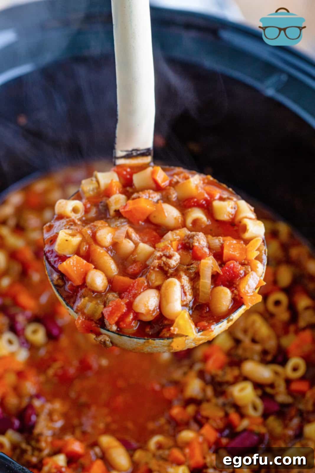 a silver ladle holding up a serving of pasta e fagioli over a slow cooker. 