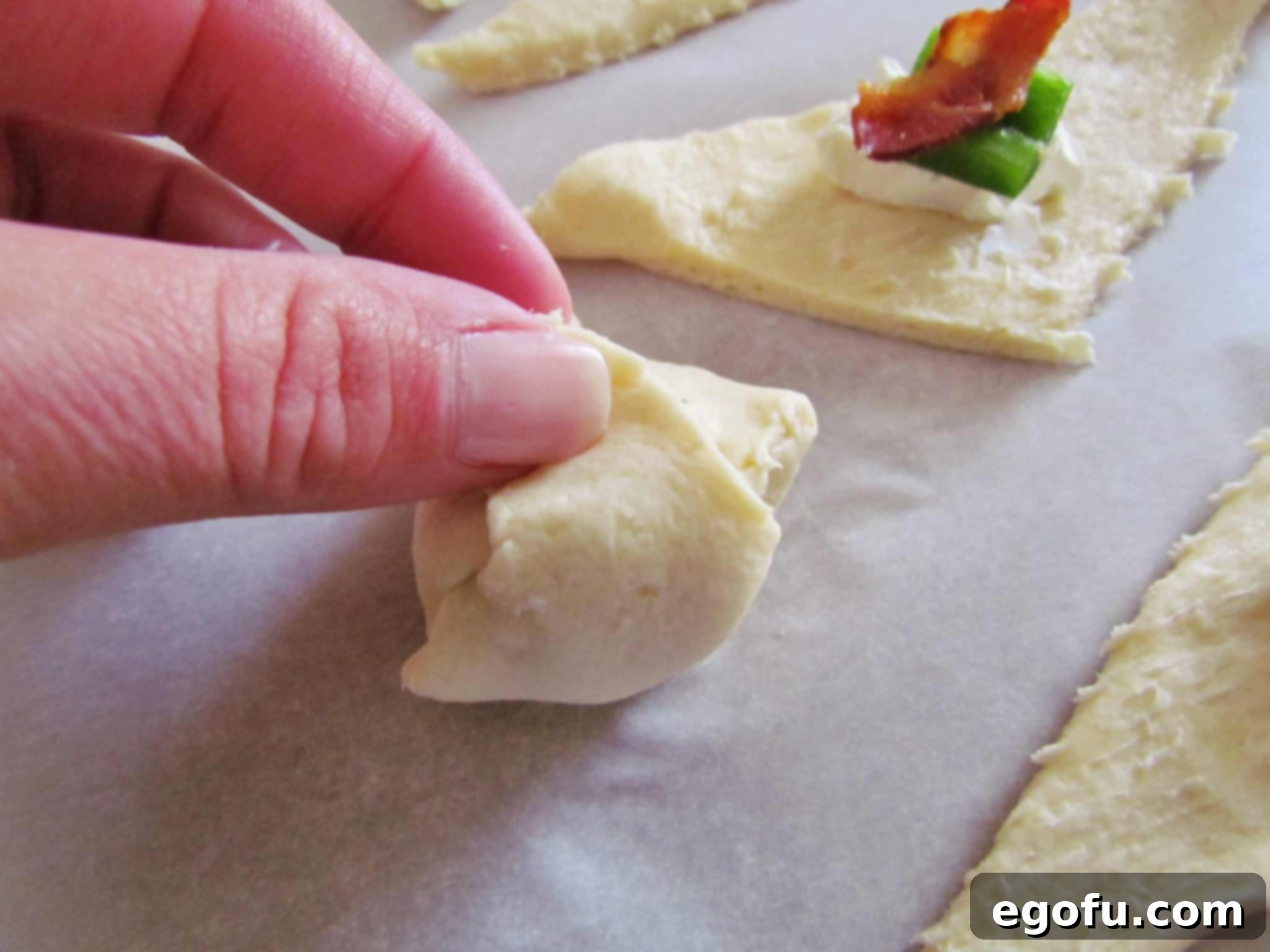 Zesty Jalapeño Delights 8 Hands carefully rolling up a crescent roll triangle, sealing in the creamy filling to create a perfect appetizer bundle.