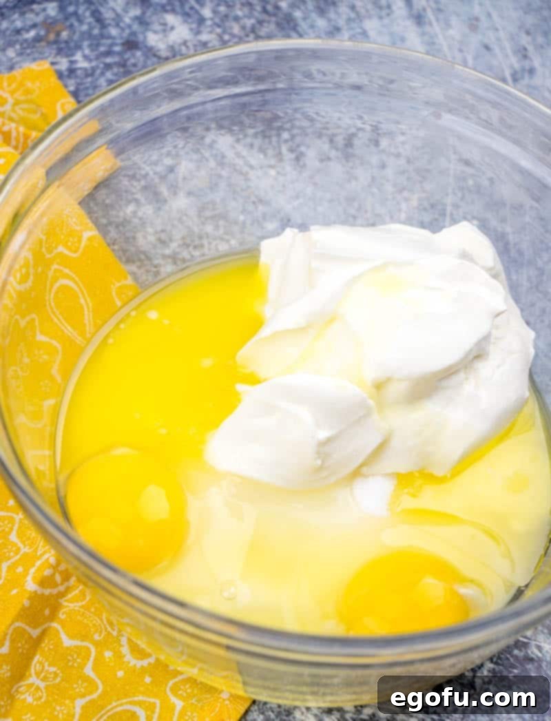 Melted butter, eggs, sugar, and sour cream are thoroughly combined in a medium bowl, creating a smooth and creamy batter base.