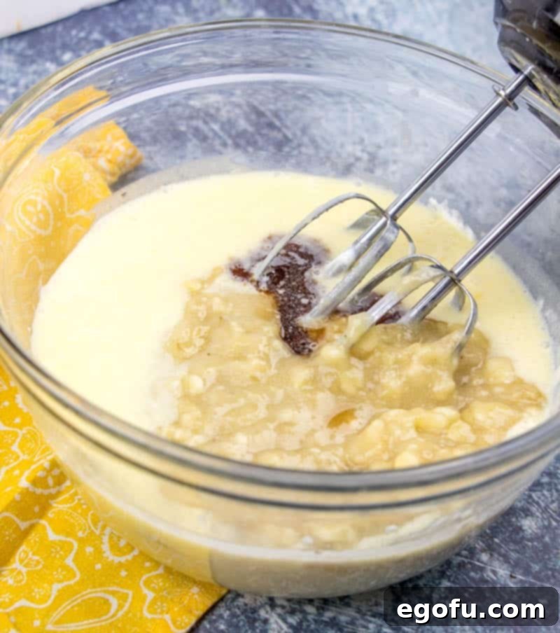 Mashed bananas and fragrant vanilla extract are carefully added to the cake batter, which is being mixed with an electric mixer to ensure even distribution.