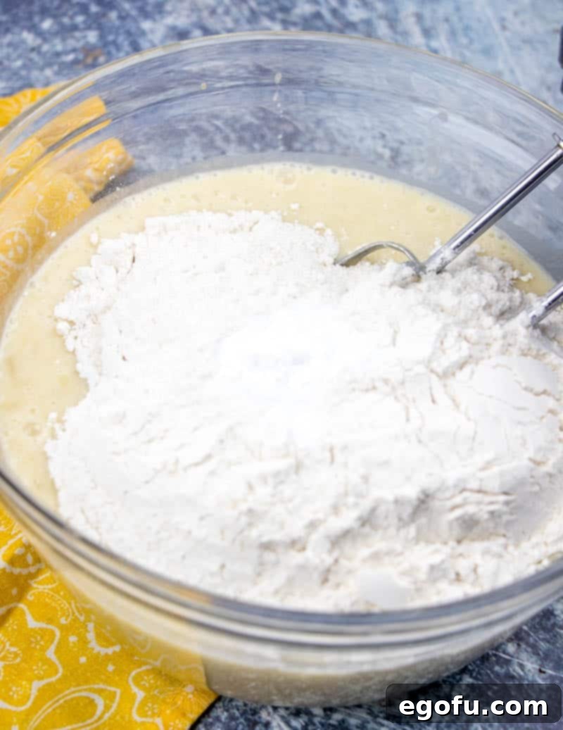All-purpose flour and baking soda are being gently added to the banana cake batter, ensuring a light and even mixture as it's folded in.