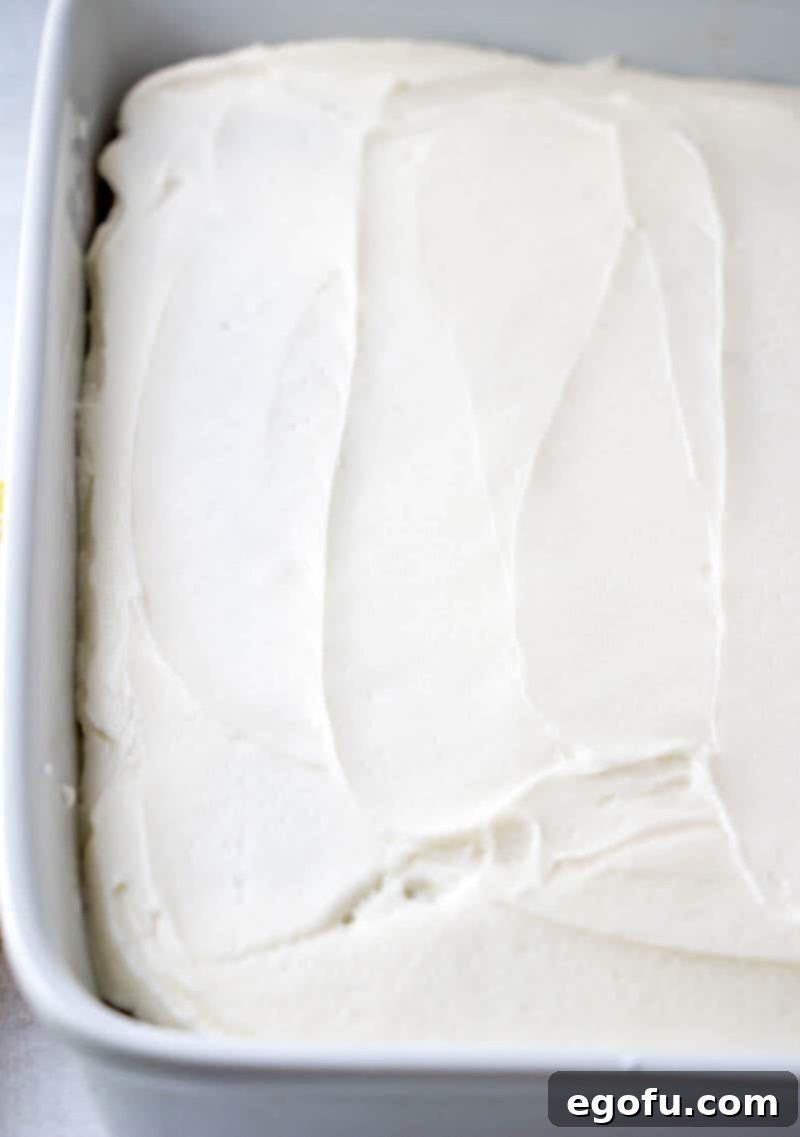 A freshly baked banana cake sits in its baking dish, beautifully frosted with smooth, creamy vanilla frosting, ready to be sliced and served.