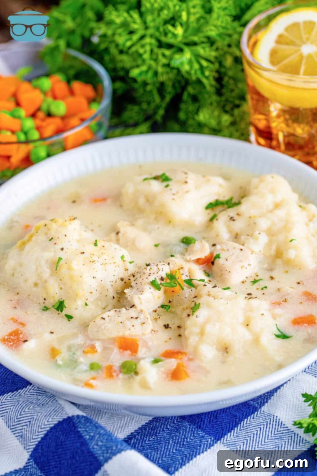 chicken and dumplings in a white bowl with a glass of iced tea in the background along with fresh parsley. 