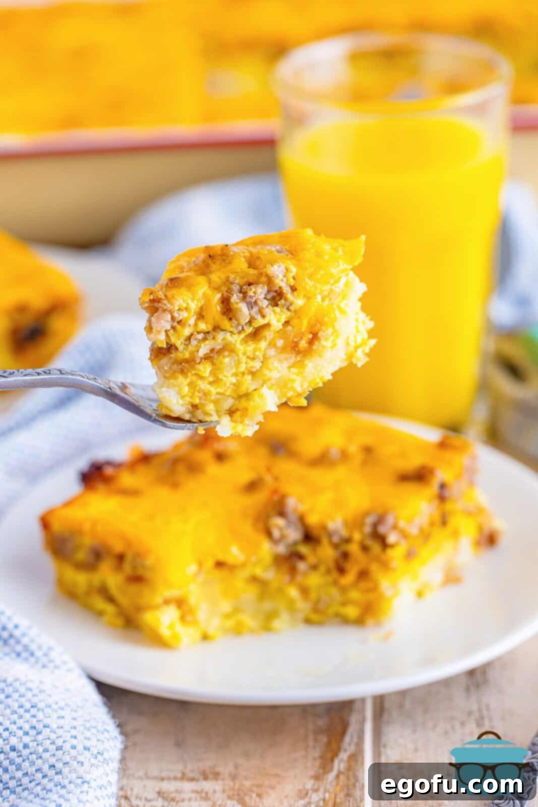 A fork holding up a small serving of golden-brown sausage hash brown casserole over a white plate, showcasing its layers.