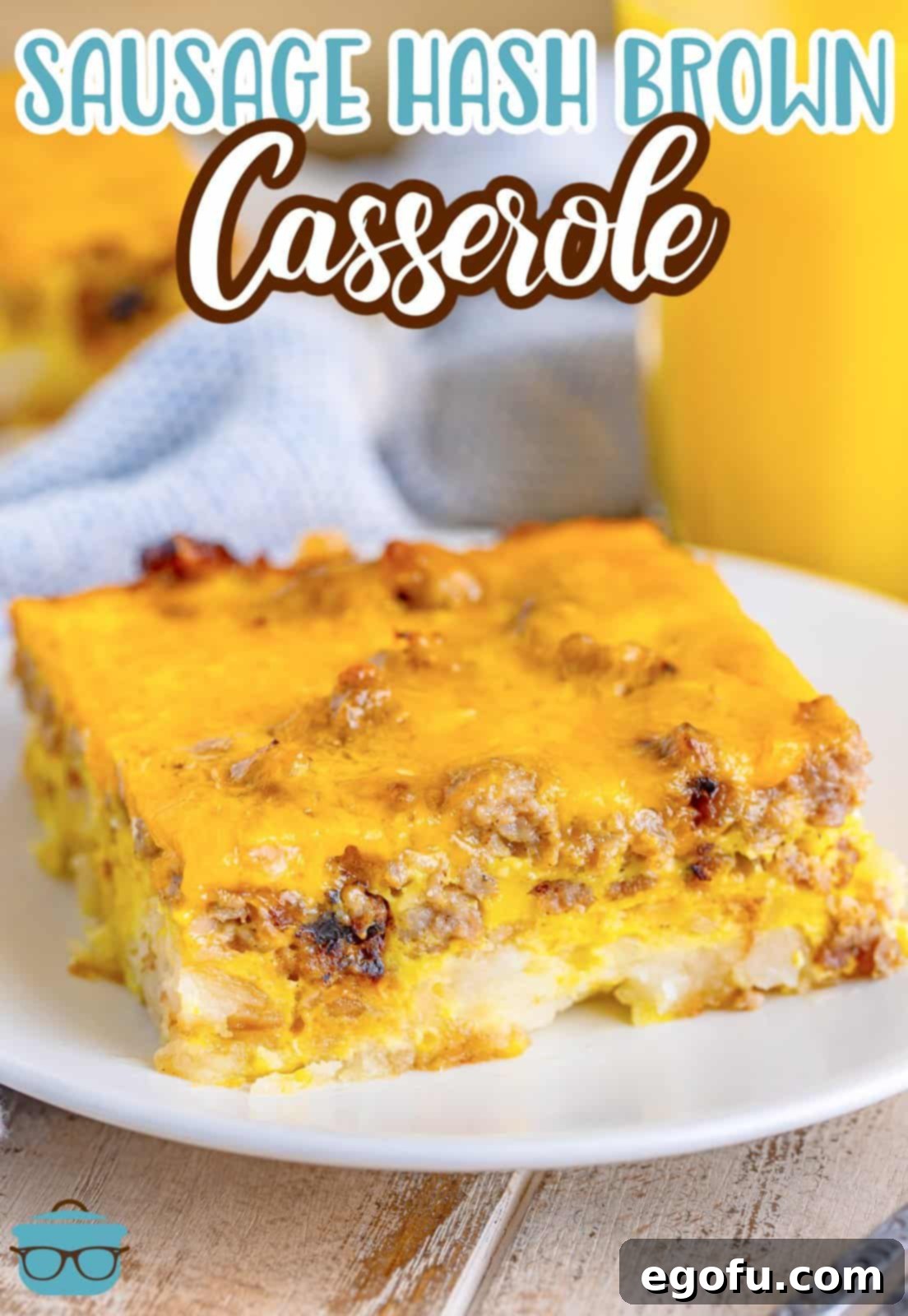 A perfectly baked slice of sausage hash brown casserole on a small round white plate, with a glass of orange juice blurred in the background.