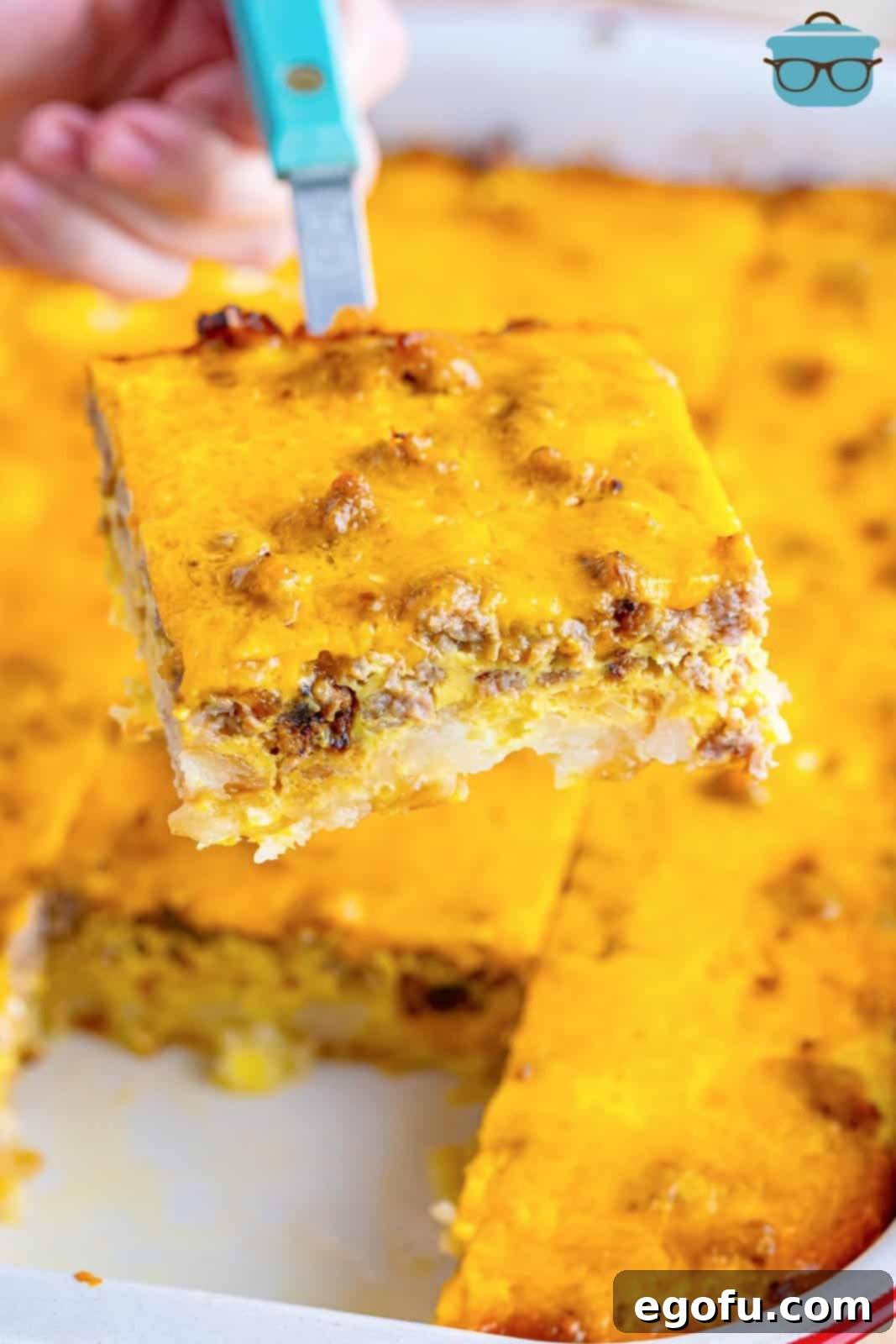 A spatula serving a hearty slice of sausage hash brown casserole from the baking dish.