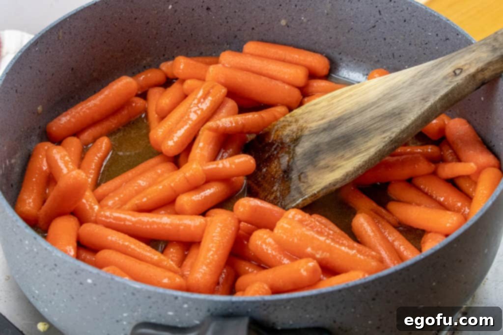 Maple Kissed Carrots 6 Fresh baby carrots being added to a large skillet already containing the warm, melted maple syrup, brown sugar, and butter glaze, prepared for gentle tossing.