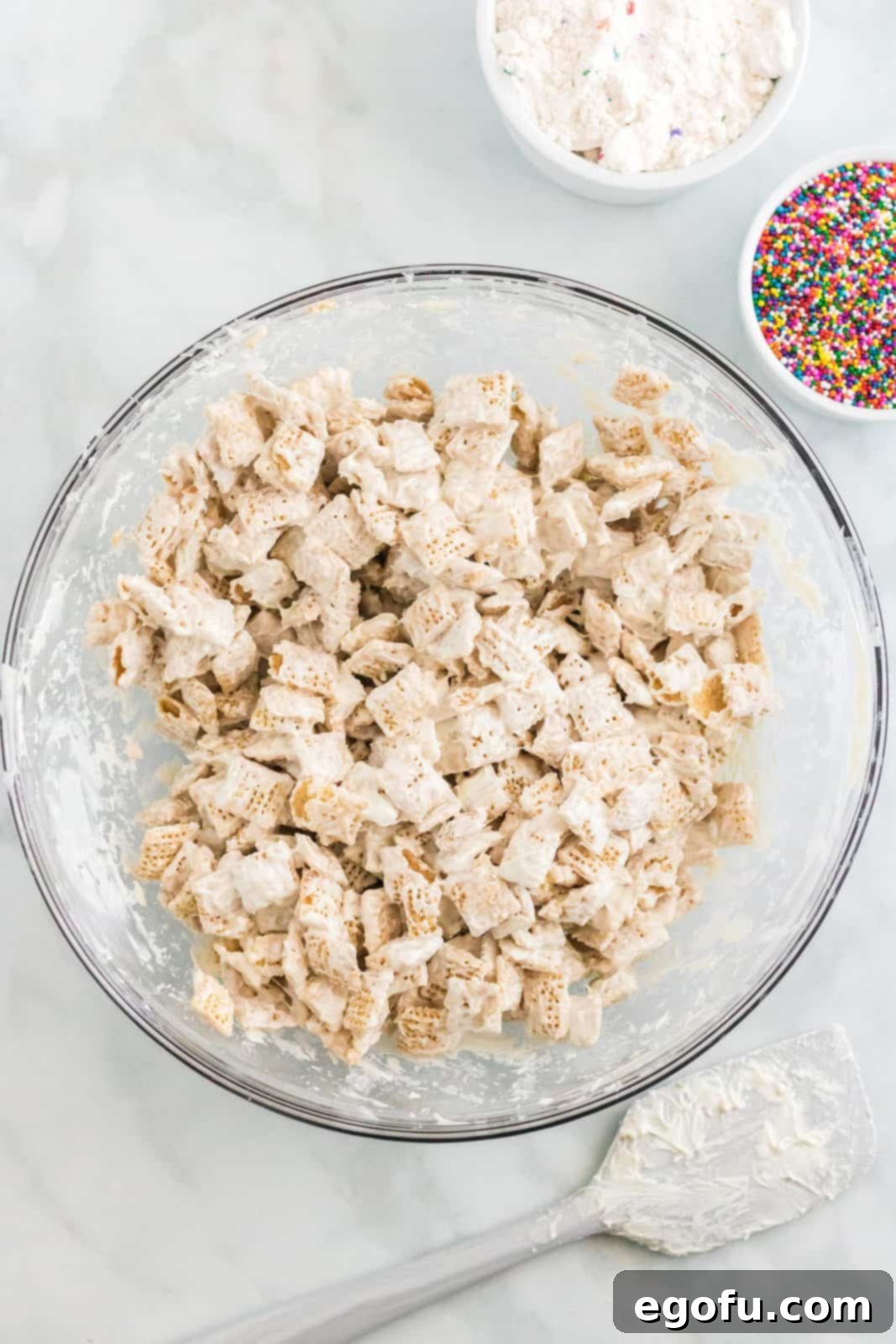 Celebration Confetti Crunch 6 Rice Chex cereal being gently stirred and coated with melted white candy in a large mixing bowl using a spatula.