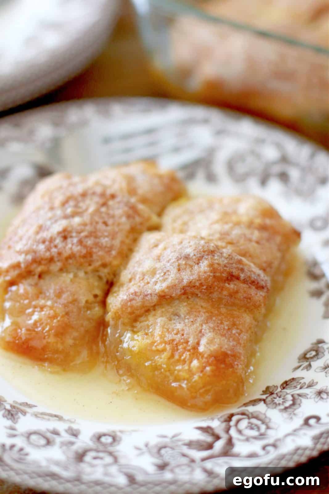 Sweet Apple Pockets 2 Two golden-brown apple cinnamon crescent roll dumplings, served on a rustic brown and white plate, ready to be enjoyed as a comforting dessert.