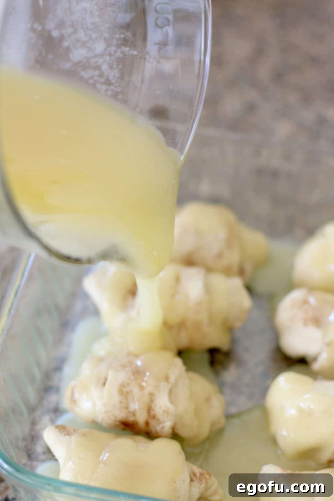 Sweet Apple Pockets 11 A golden butter and sugar mixture being poured directly over the tops of the crescent-wrapped apple dumplings in a glass baking dish.