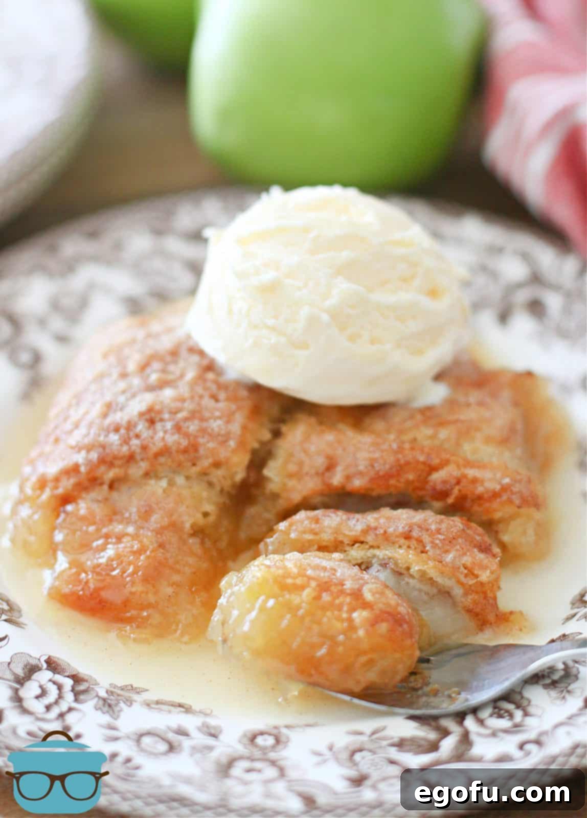 Sweet Apple Pockets 14 Two warm apple dumplings adorned with a melting scoop of vanilla ice cream and drizzled with rich sauce, ready to be enjoyed on a brown and white plate.