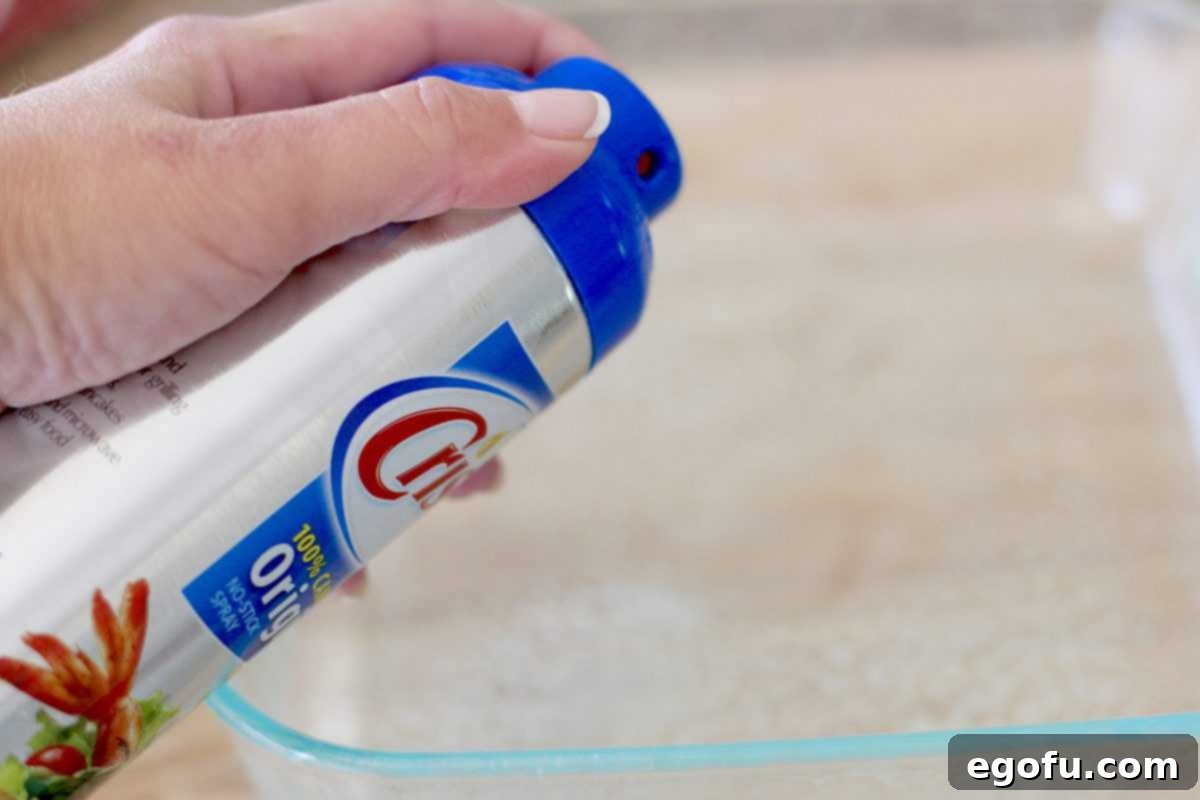 Sweet Apple Pockets 5 A hand spraying a clear glass 8-inch square baking dish with Crisco nonstick cooking spray, preparing it for the apple dumplings.