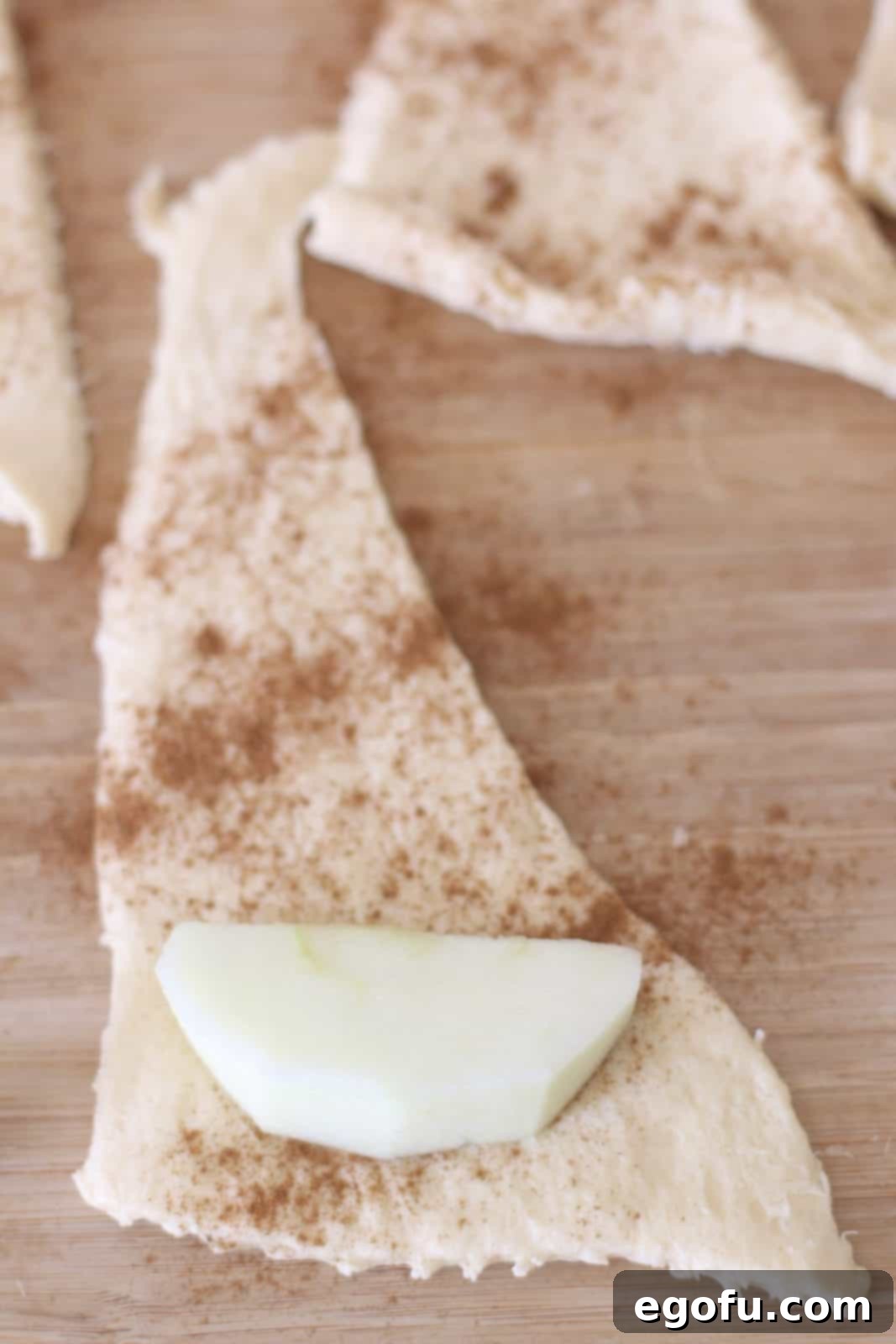 Sweet Apple Pockets 8 A single slice of apple placed on the wider end of a cinnamon-dusted crescent roll dough triangle, poised to be rolled into a dumpling.